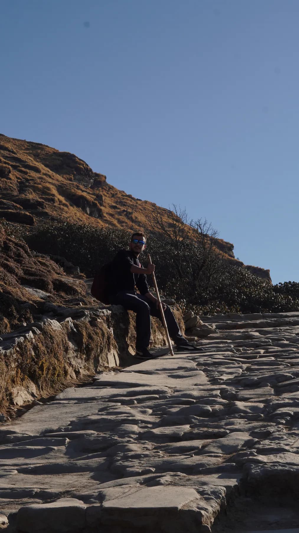 Trekker resting with a walking stick on the stone trail toward Tungnath