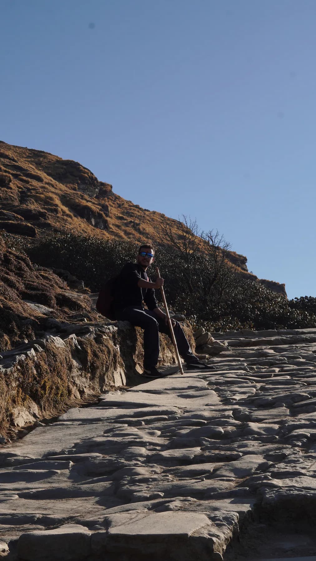 Trekker resting with a walking stick on the stone trail to Tungnath